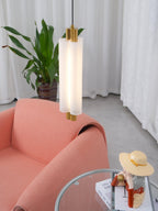 Close view of the frosted cylinder and gold cap of a Clérachic pendant, above a coral armchair and a figurine on books.