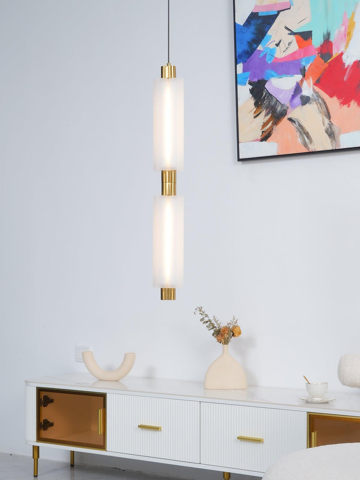 A two-head Clérachic pendant with gold joints hangs above a white fluted sideboard, beside a bold abstract painting.