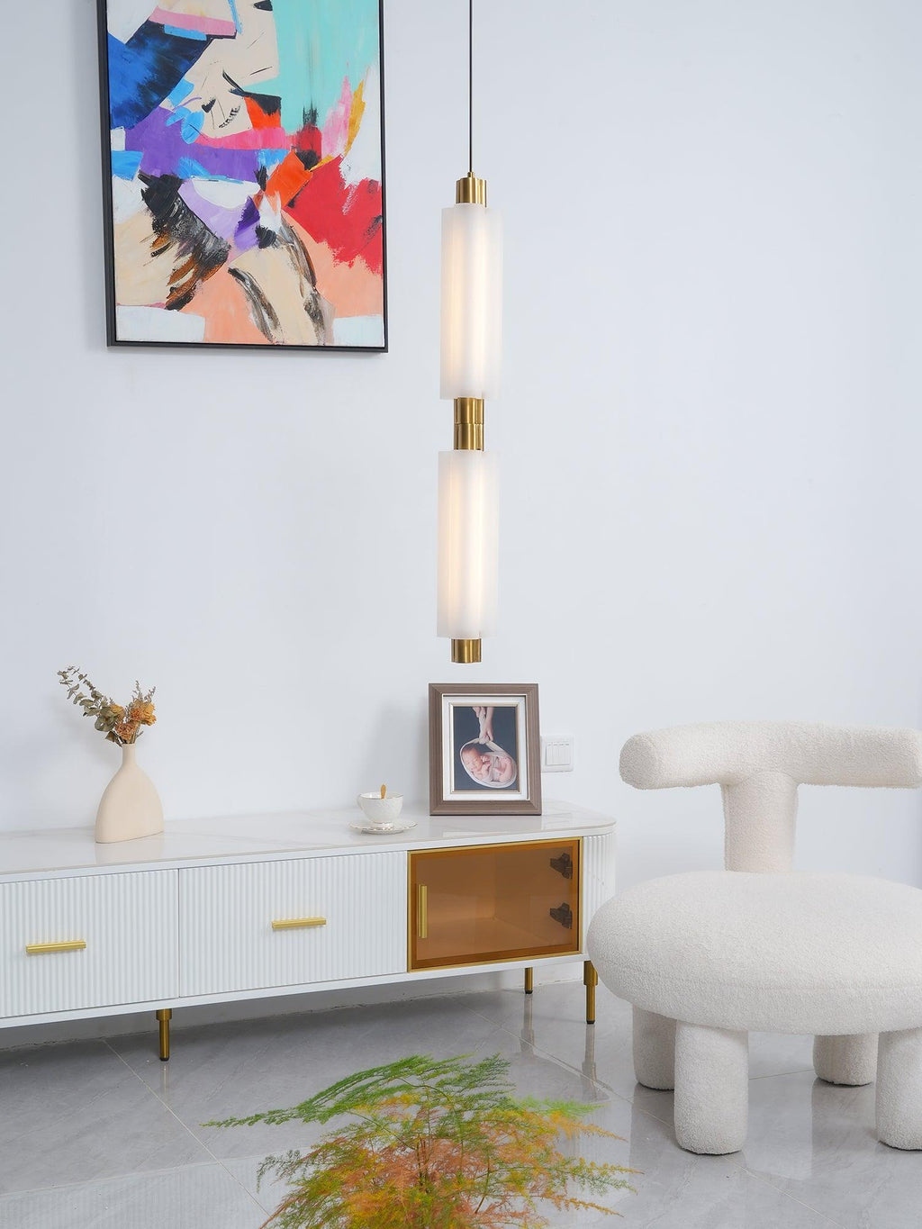 A Clérachic pendant with two frosted heads hangs by an abstract painting, above a white sideboard and a boucle stool.