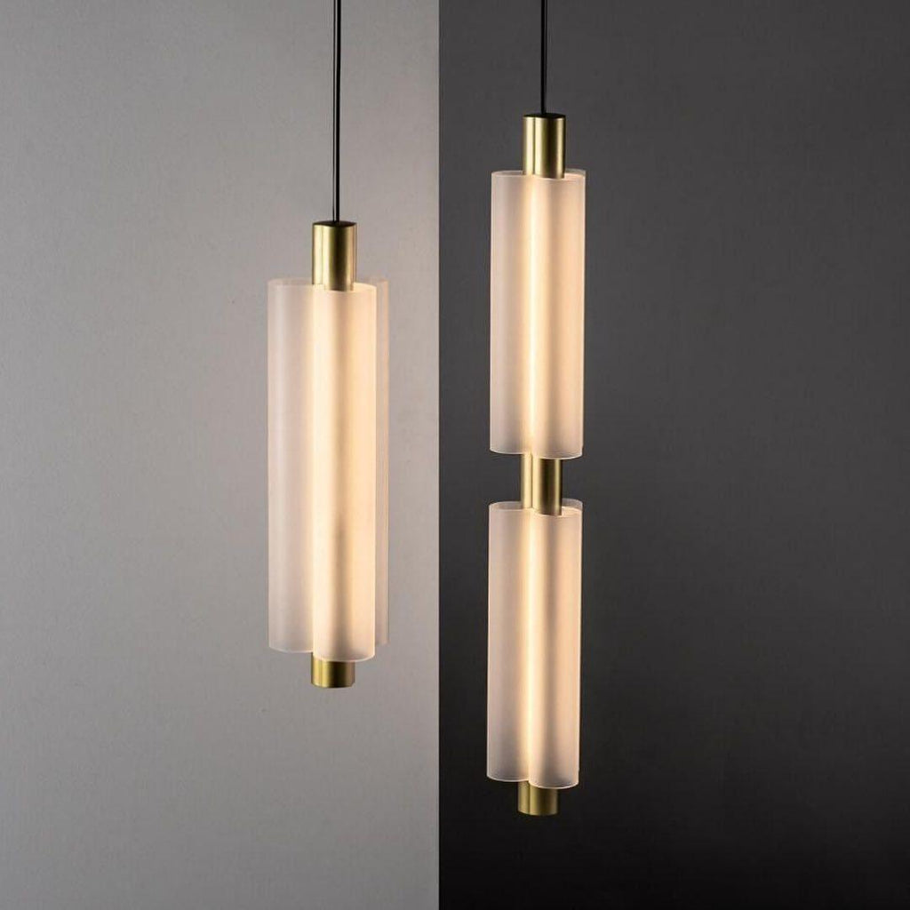 Two gold-ended Clérachic pendants, a single and a double, glow against a split grey and charcoal wall.
