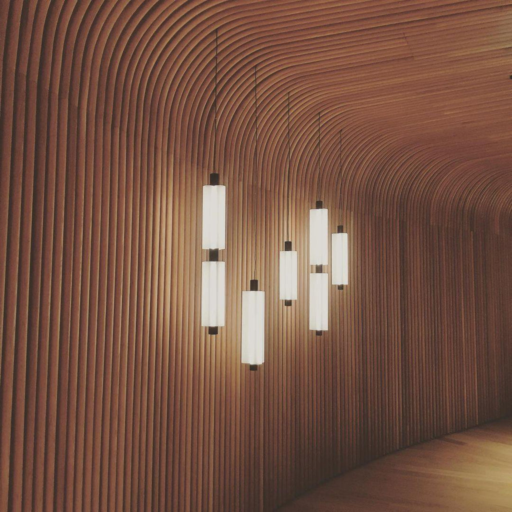 Clérachic pendants of different heights glow warm against a sweeping wall of curved wooden slats.