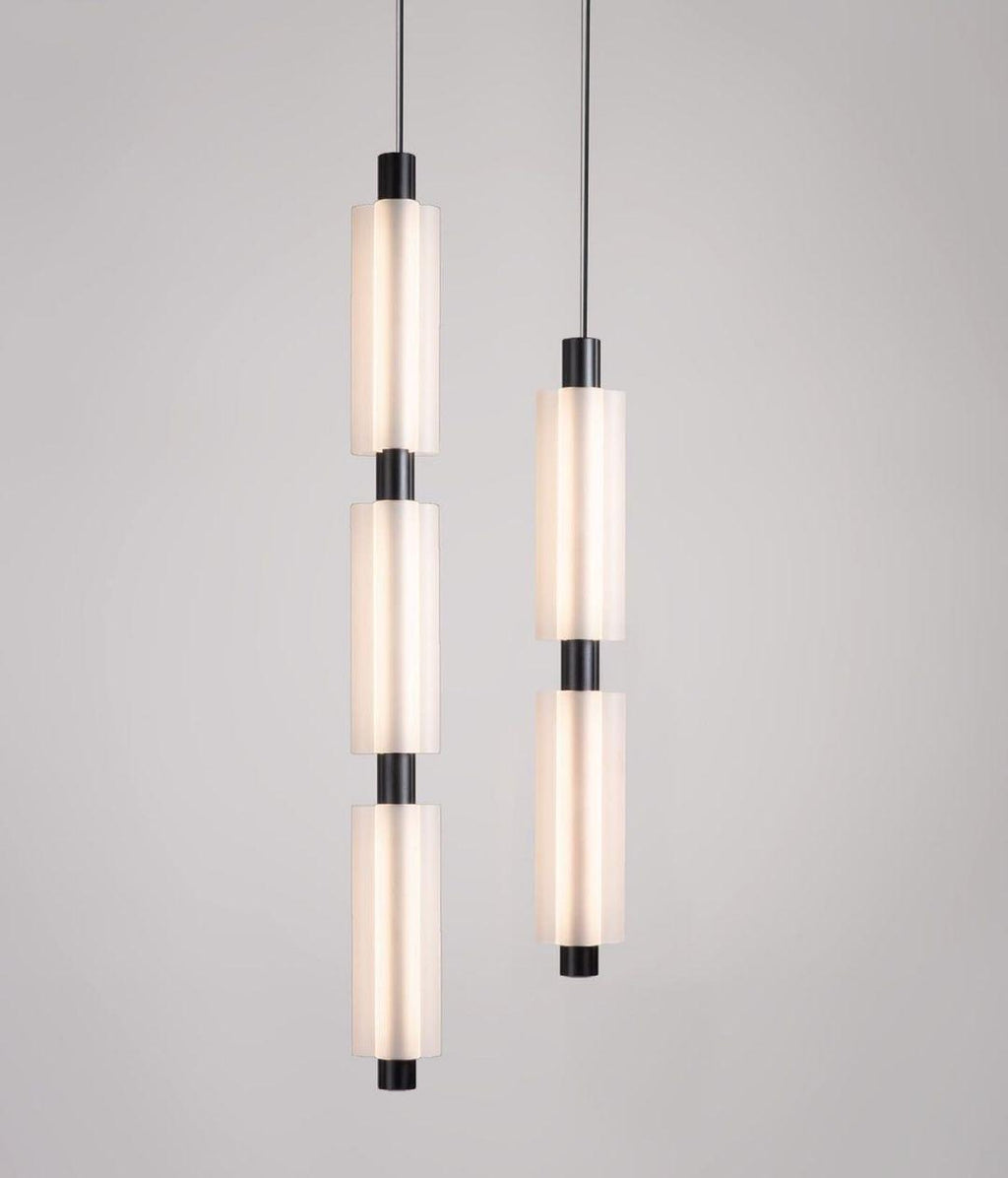 Two black-fitted Clérachic pendants, a three-head and a two-head, hang side by side against a pale grey wall.