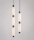 Two black-fitted Clérachic pendants, a three-head and a two-head, hang side by side against a pale grey wall.