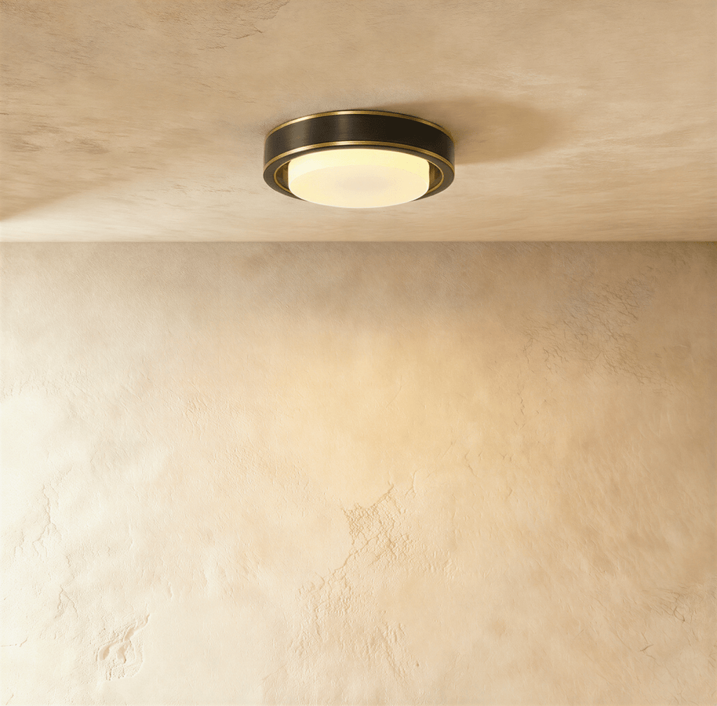 Clérachic round flush ceiling light with a dark bronze-black band, thin brass trim and a lit frosted glass cover on plaster.