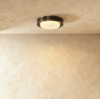 Clérachic round flush ceiling light with a dark bronze-black band, thin brass trim and a lit frosted glass cover on plaster.