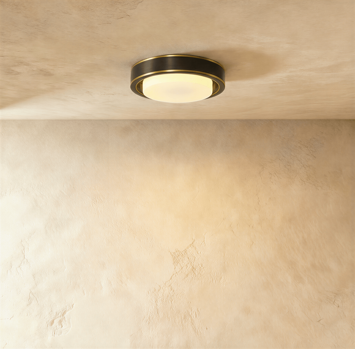 Clérachic round flush ceiling light with a dark bronze-black band, thin brass trim and a lit frosted glass cover on plaster.