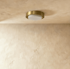 Clérachic compact flush ceiling light, brushed brass ring around an unlit white frosted glass cover, on a limewashed ceiling.