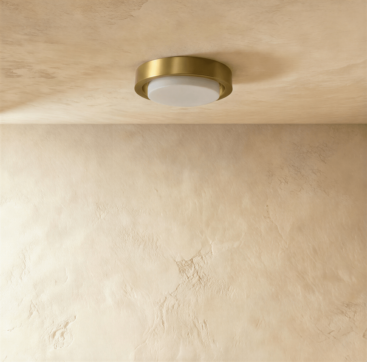 Clérachic compact flush ceiling light, brushed brass ring around an unlit white frosted glass cover, on a limewashed ceiling.