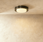 Clérachic larger round flush ceiling light in a dark black finish with fine brass edging and a glowing frosted glass cover.