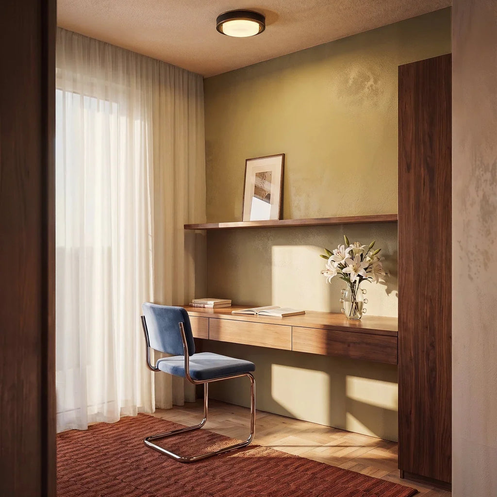 Clérachic black flush ceiling light with brass trim above a home desk nook with sheer curtains, a blue velvet chair and lilies.