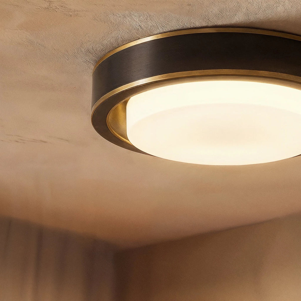 Close view of a Clérachic round ceiling light, black band edged in brass, with the frosted glass cover glowing warmly.