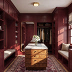 Clérachic brass flush ceiling light in a deep burgundy dressing room with an island of burr wood drawers and a marble top.