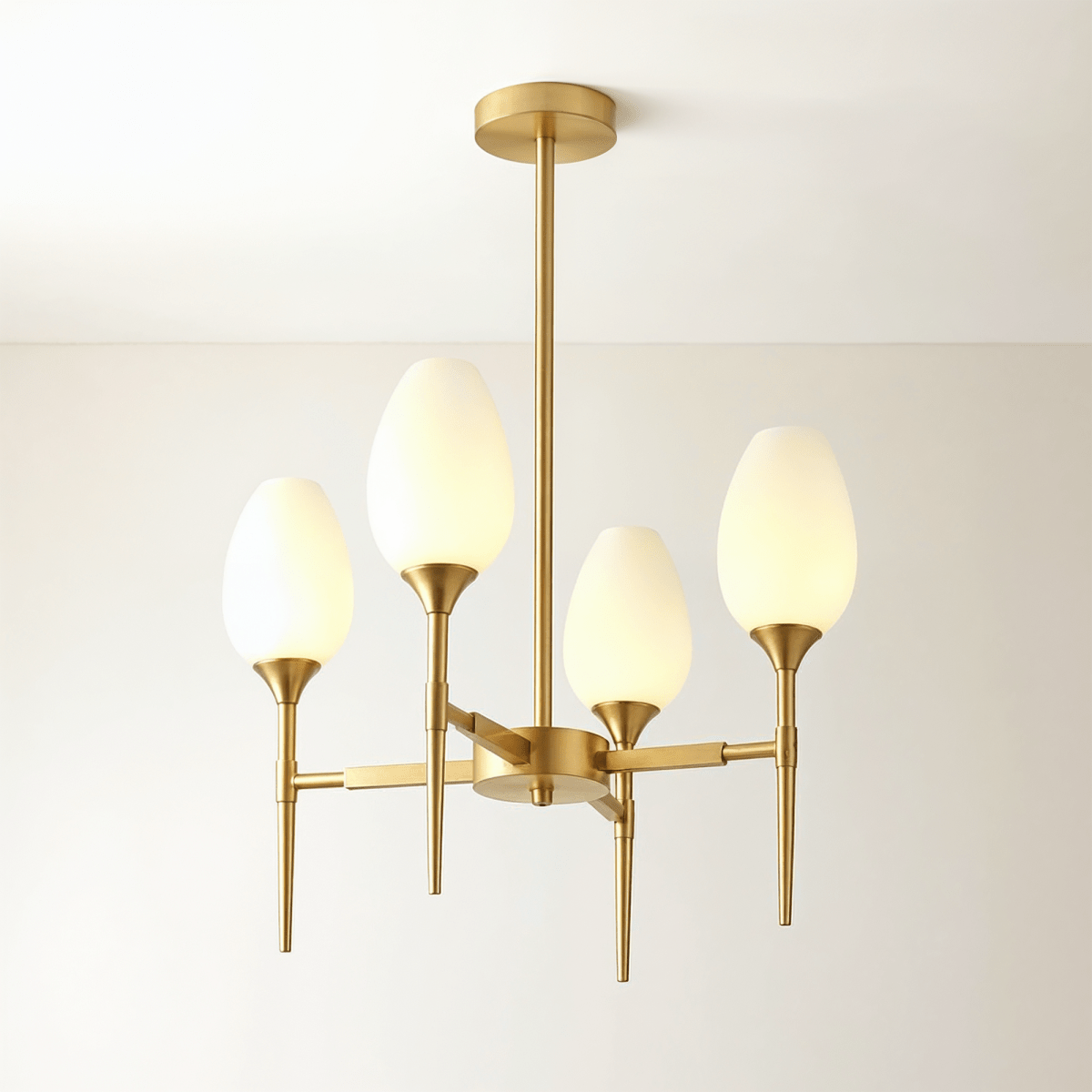 Clérachic four-arm brass chandelier with tulip-shaped frosted glass shades, lit warm, on a central brass stem and round ceiling plate.