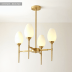 Clérachic four-arm brass chandelier with frosted tulip shades glowing warm on a brass stem against a cream wall and ceiling.