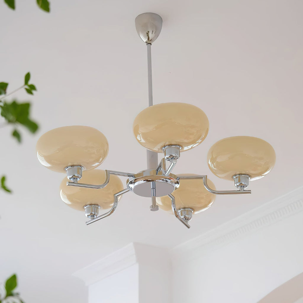 Unlit chrome Clérachic chandelier hanging from a white ceiling with cornice, its pale beige glass heads spread on angled arms.