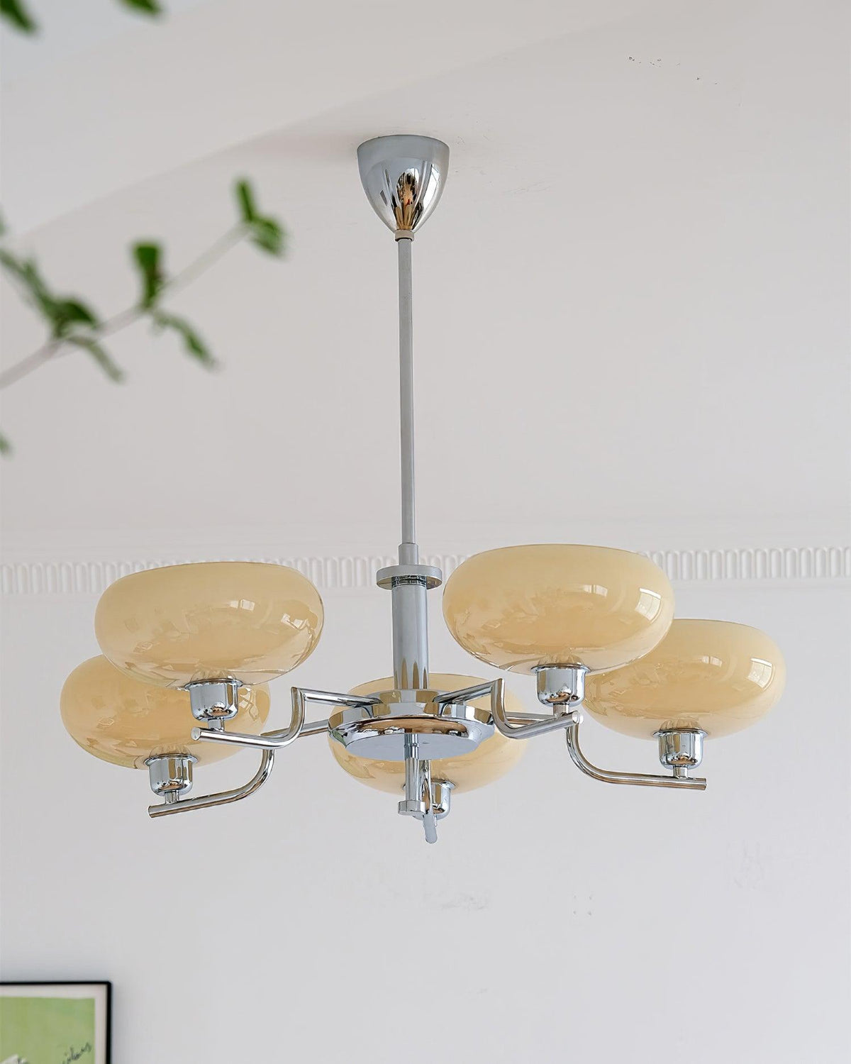 Chrome and beige Clérachic chandelier seen from slightly below, its glass heads a warm sand tone against a white wall.