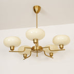 Gold Clérachic chandelier lit against a white ceiling, creamy glass domes on flat brass arms beneath a gold cone canopy.