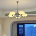 Chrome Clérachic chandelier lit high in a room with a cream ceiling and a ceiling vent, an arched window with a mountain view below.