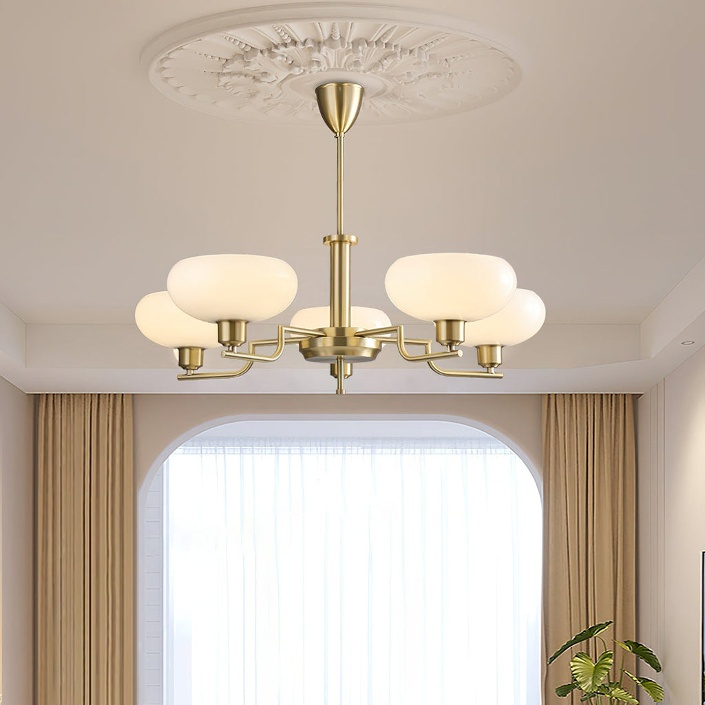 Lit gold Clérachic chandelier below a plaster ceiling rose in a room with an arched window and tan curtains.