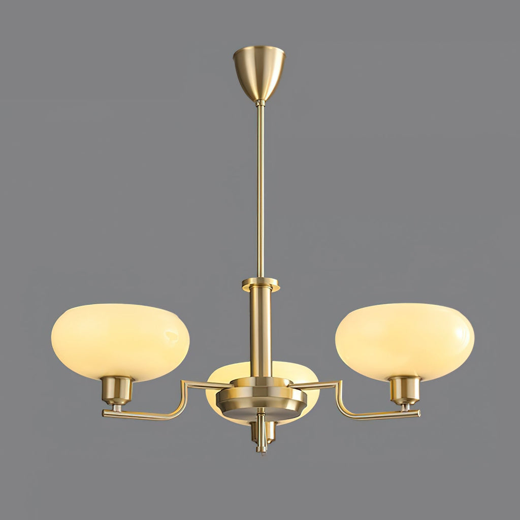 Three-head gold Clérachic chandelier lit on a grey backdrop, creamy glass domes on brass arms.