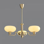 Three-head gold Clérachic chandelier lit on a grey backdrop, creamy glass domes on brass arms.