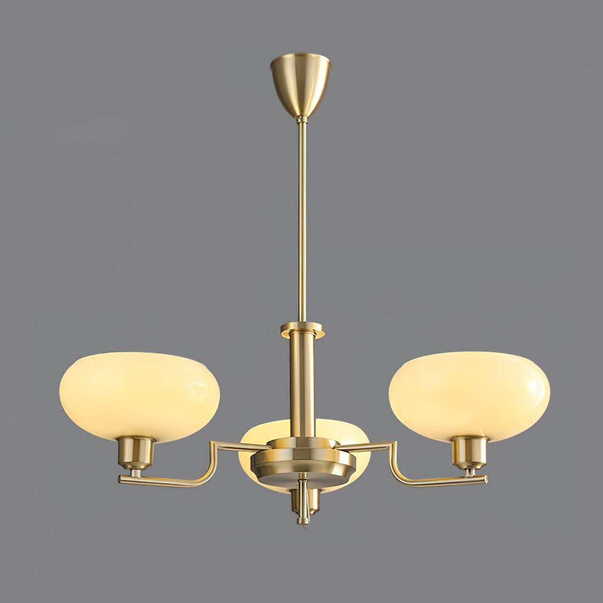 Three-head gold Clérachic chandelier lit on a grey backdrop, creamy glass domes on brass arms.