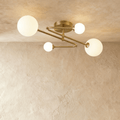 Clérachic four-head ceiling light with brass-toned arms zigzagging from a round canopy, each arm ending in a frosted glass globe.