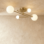 Clérachic four-head ceiling light with brass-toned arms zigzagging from a round canopy, each arm ending in a frosted glass globe.