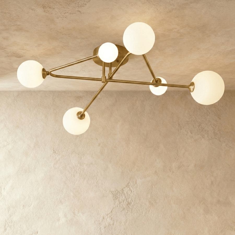Clérachic six-head ceiling light with slim brass-toned arms crossing from a round canopy, frosted white glass globes lit.