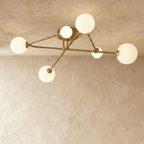Clérachic six-head ceiling light with slim brass-toned arms crossing from a round canopy, frosted white glass globes lit.