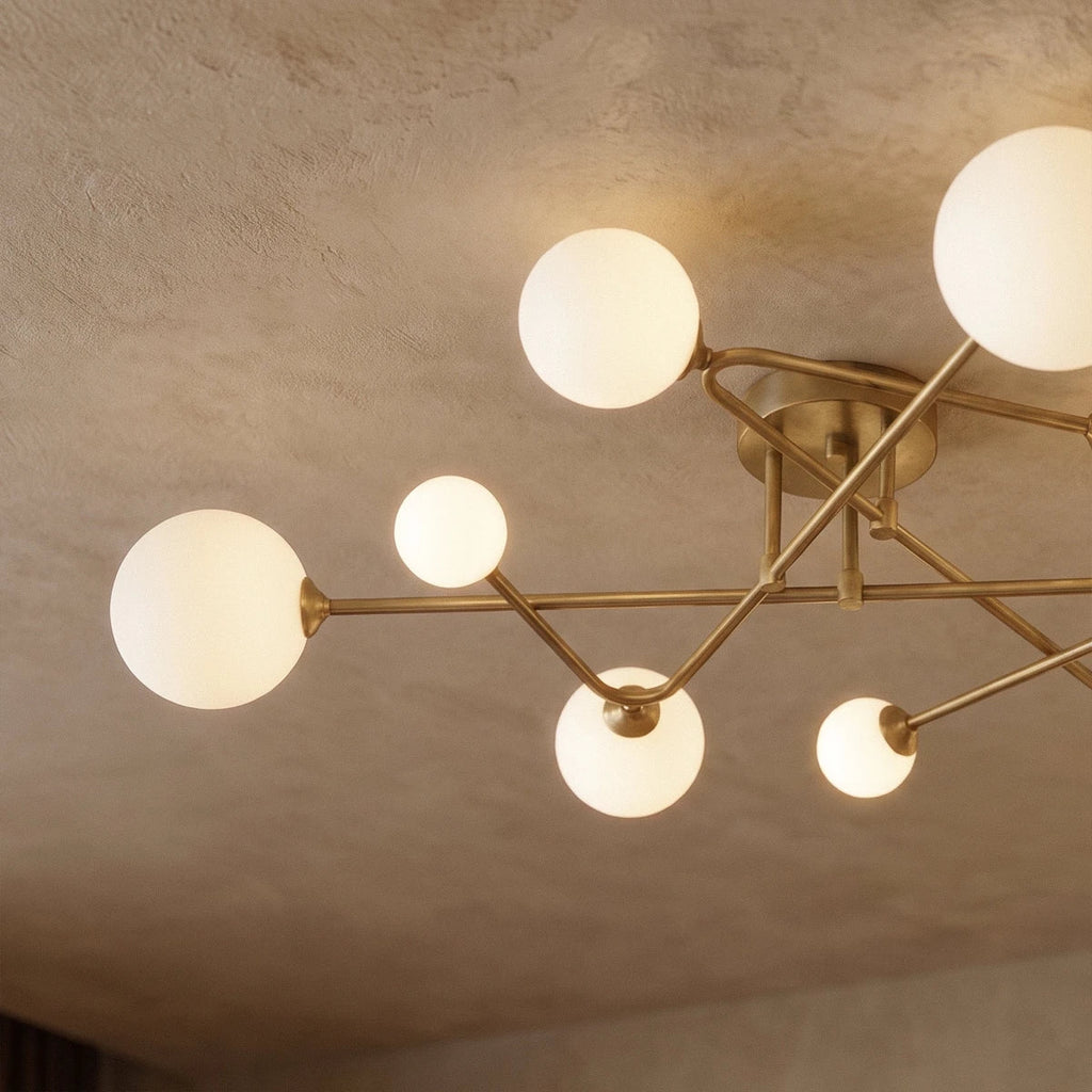 Close view of a Clérachic nine-head ceiling light, showing slim brass-toned arms, small canopy and glowing frosted glass globes.