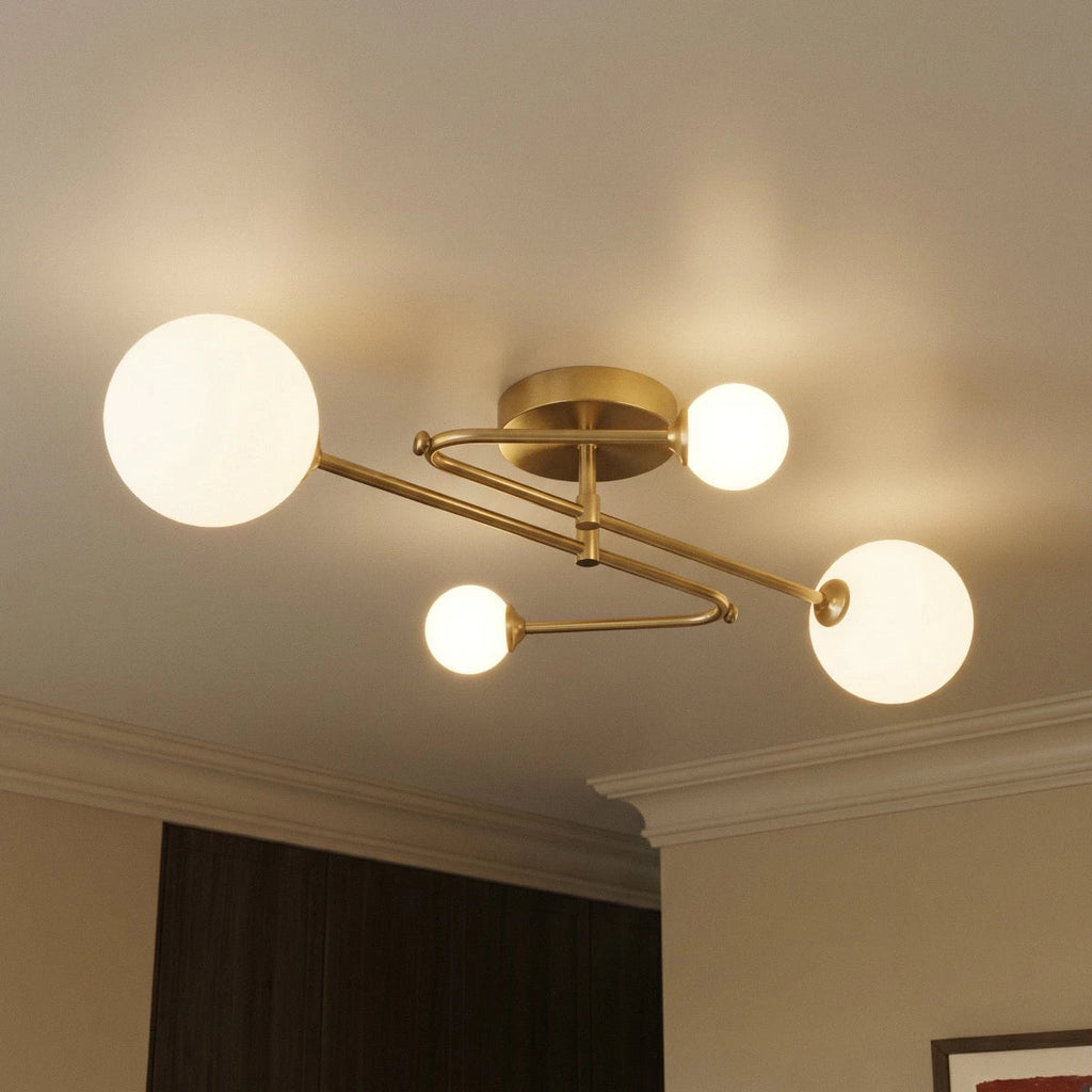 Close view of a Clérachic four-head ceiling light, showing its looping brass-toned arms, round canopy and glowing frosted globes.