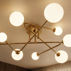 Close view from below of a Clérachic nine-head ceiling light, showing crossed brass-toned arms and frosted globes of varied size.
