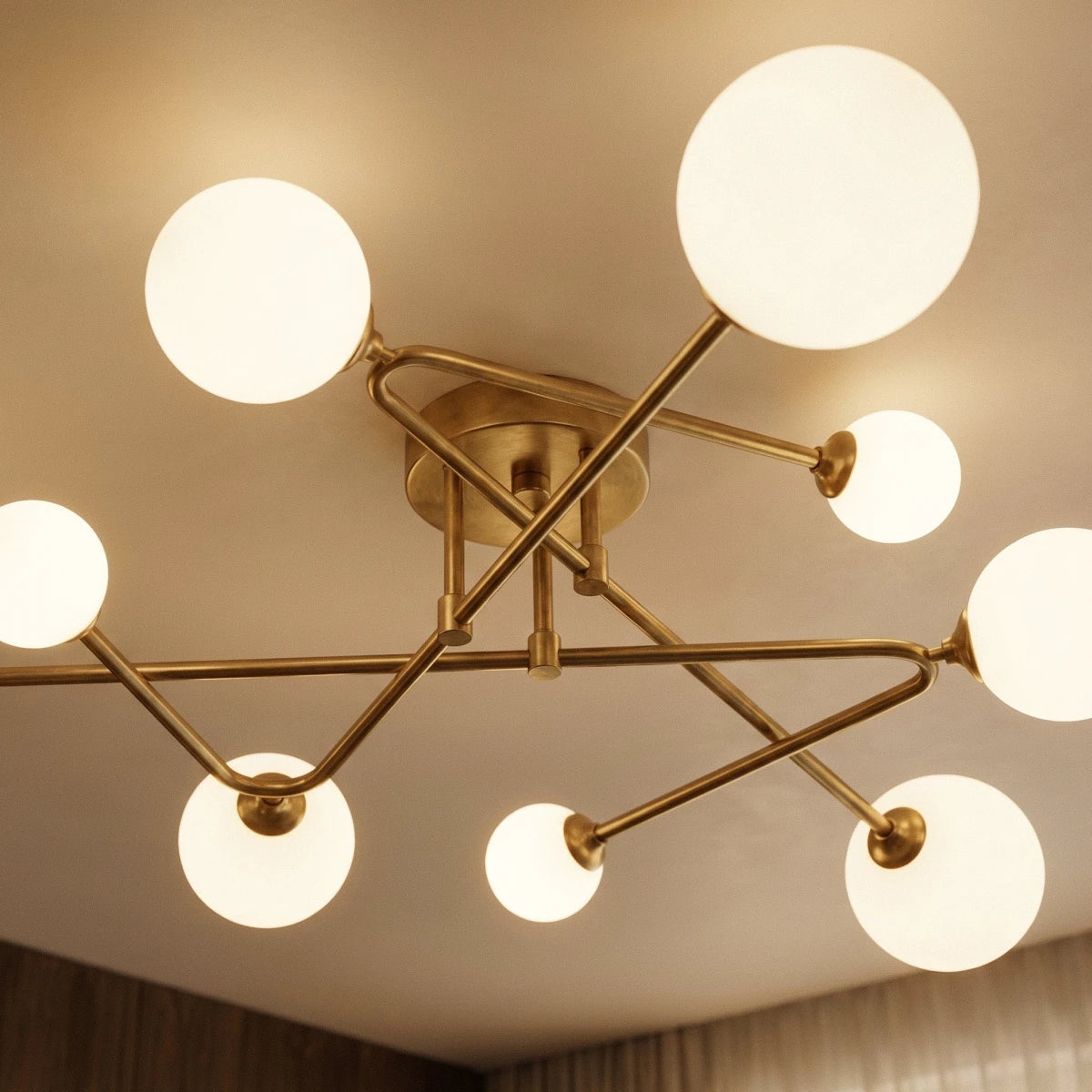 Close view from below of a Clérachic nine-head ceiling light, showing crossed brass-toned arms and frosted globes of varied size.