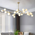 This Clérachic chandelier in gold and white hangs in a grey living room, its branches carrying frosted globes beside sheer curtains.