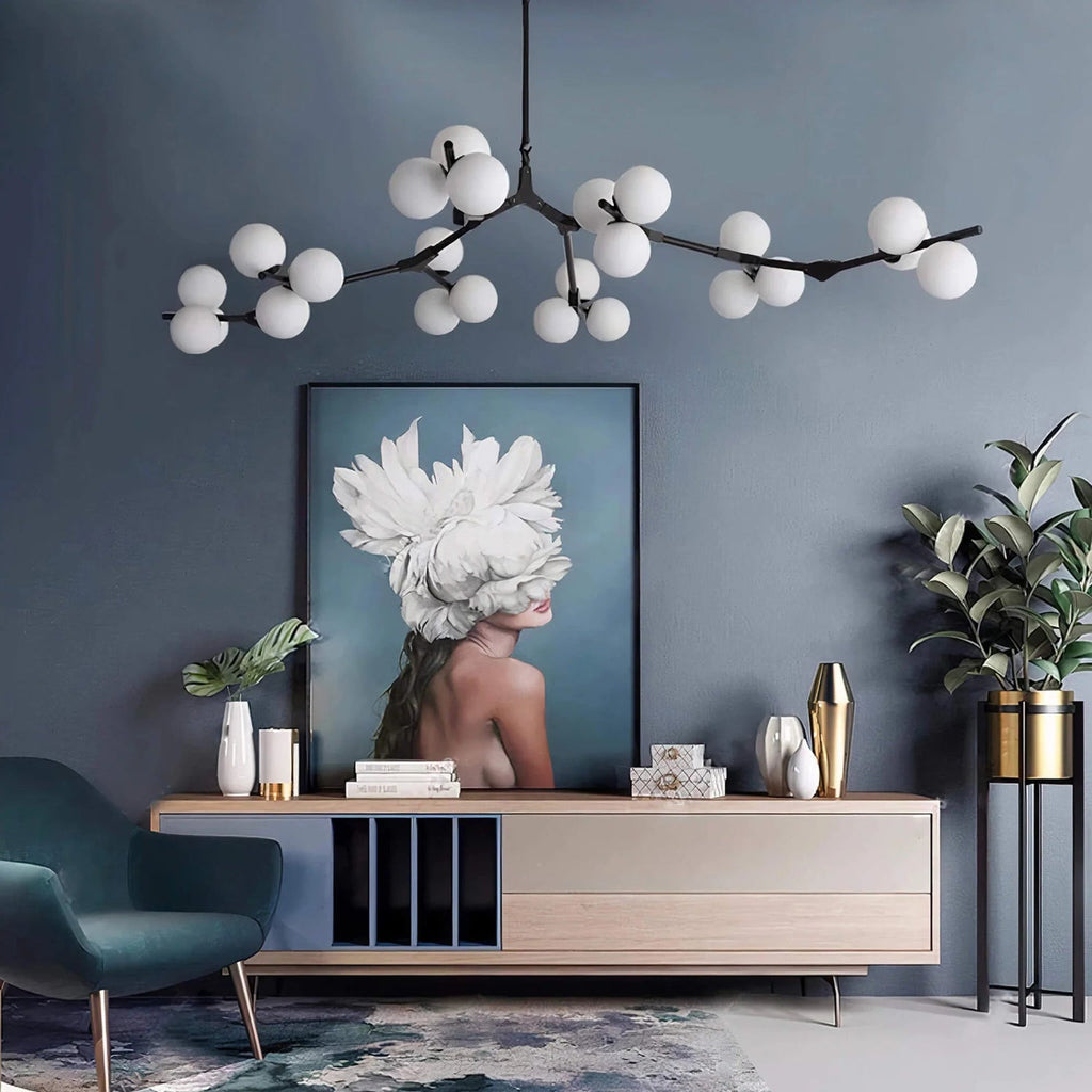 Black branching Clérachic chandelier lit above a blue-grey wall with a large portrait print, a pale sideboard and a teal armchair.