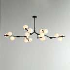 Wider black chandelier with branches spread across a pale wall, a frosted globe lit at each cluster; from Clérachic.