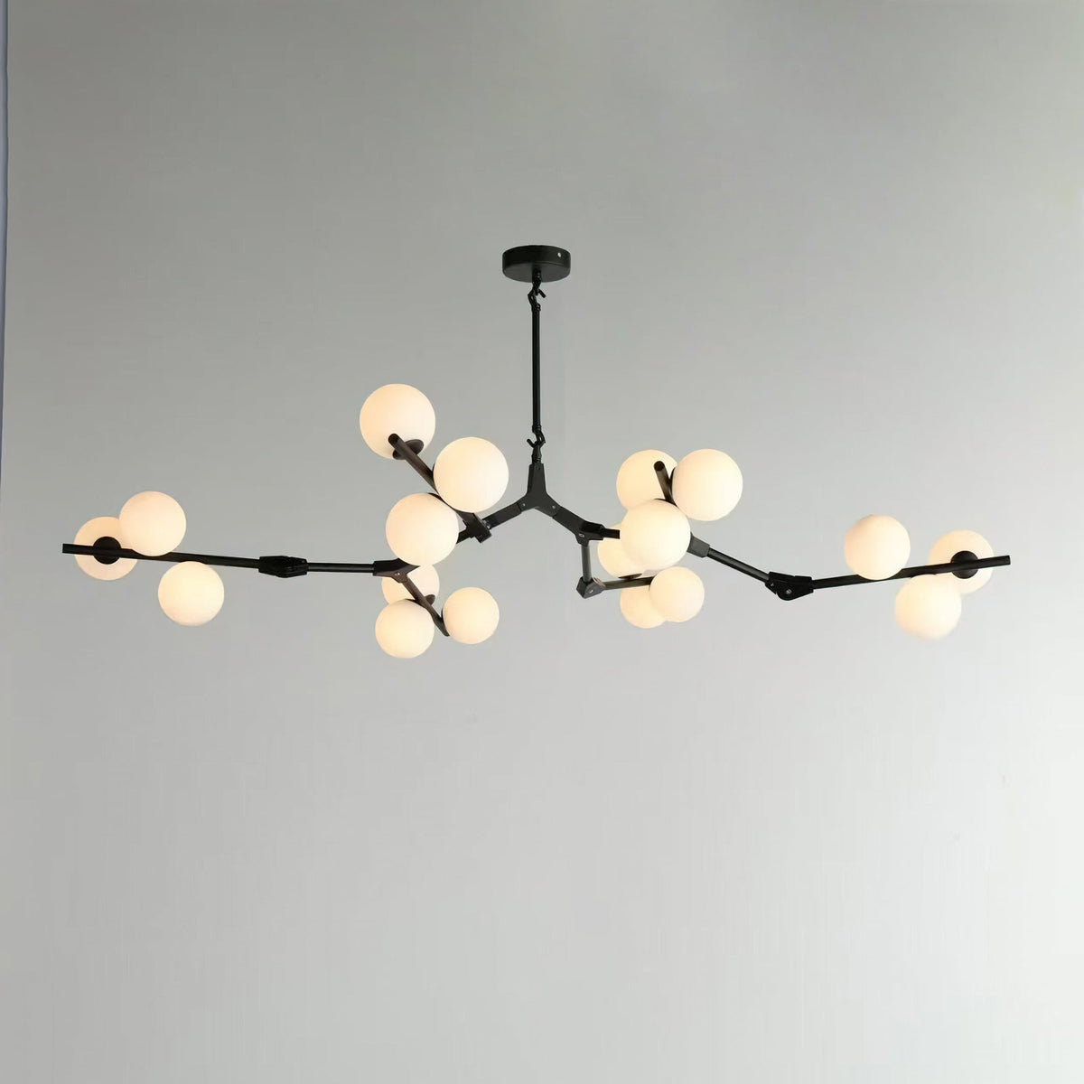 Wider black chandelier with branches spread across a pale wall, a frosted globe lit at each cluster; from Clérachic.