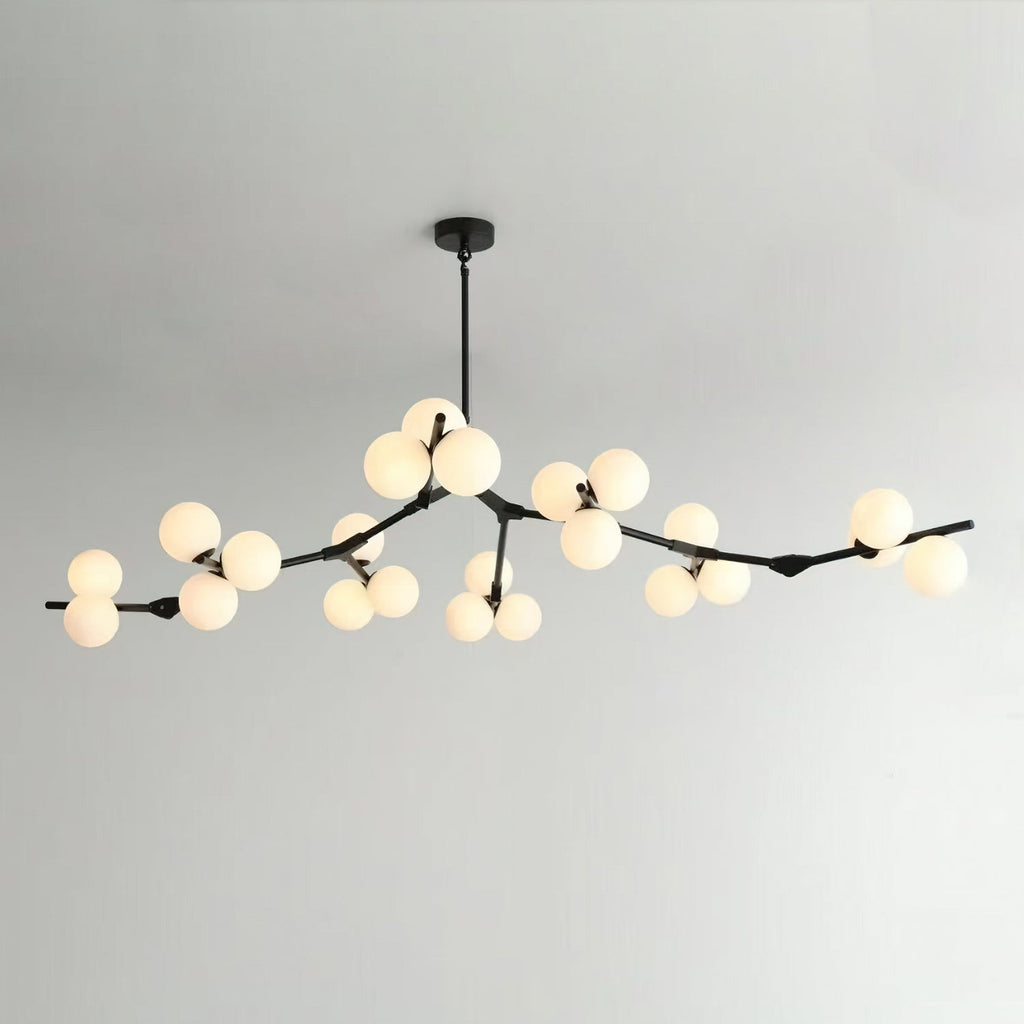 Black Clérachic chandelier on a thin rod with many lit frosted globes along long, low branches, against a pale grey wall.