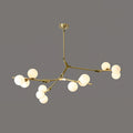 Gold and white three-armed chandelier with lit globes on thin brass branches, hung from a small gold canopy on dark grey; Clérachic.