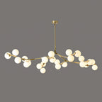 The widest gold and white Clérachic chandelier, with lit white globes clustered along its long brass branches on dark grey.