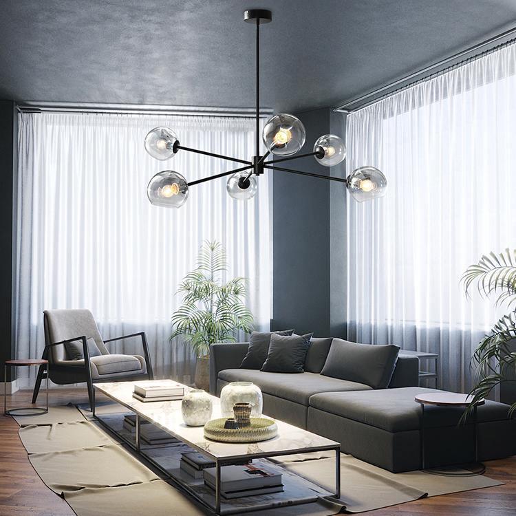 Black Clérachic chandelier with six smoked glass globes above a coffee table and a charcoal sofa, in a living room with sheer curtains.