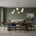 Gold-finish chandelier from Clérachic with six opal white globes above a wooden dining table with blue and green chairs, against an olive wall.