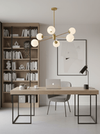 Gold chandelier from Clérachic with white globes hung above a desk with a laptop, beside a tall bookcase and a framed print.