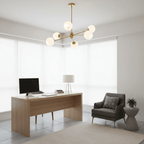 Gold six-light Clérachic chandelier with white globes in a bright corner office with a wooden desk, a monitor and a grey armchair.