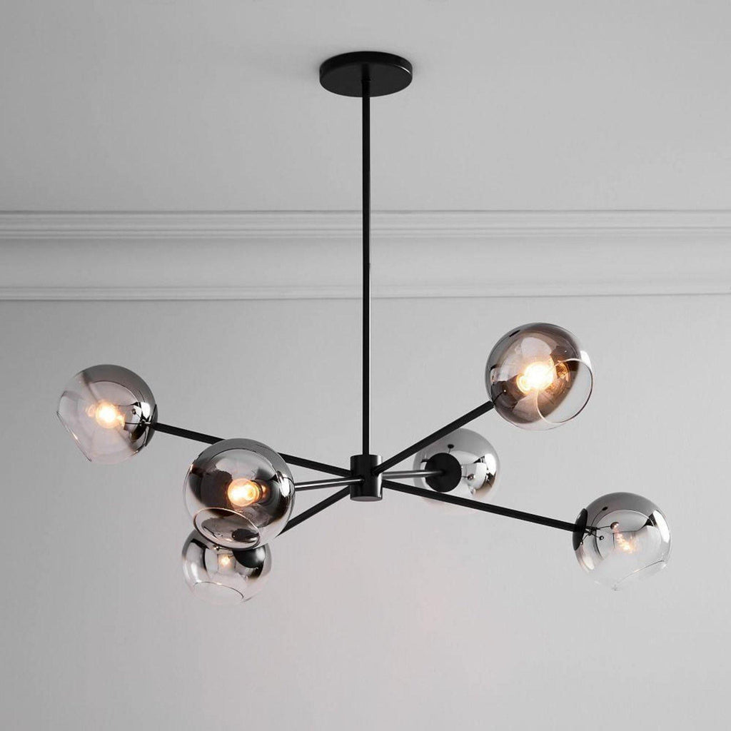 Close view of a black Clérachic chandelier with smoked glass globes, one lit, below a white ceiling with a cornice.