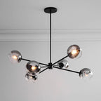 Close view of a black Clérachic chandelier with smoked glass globes, one lit, below a white ceiling with a cornice.