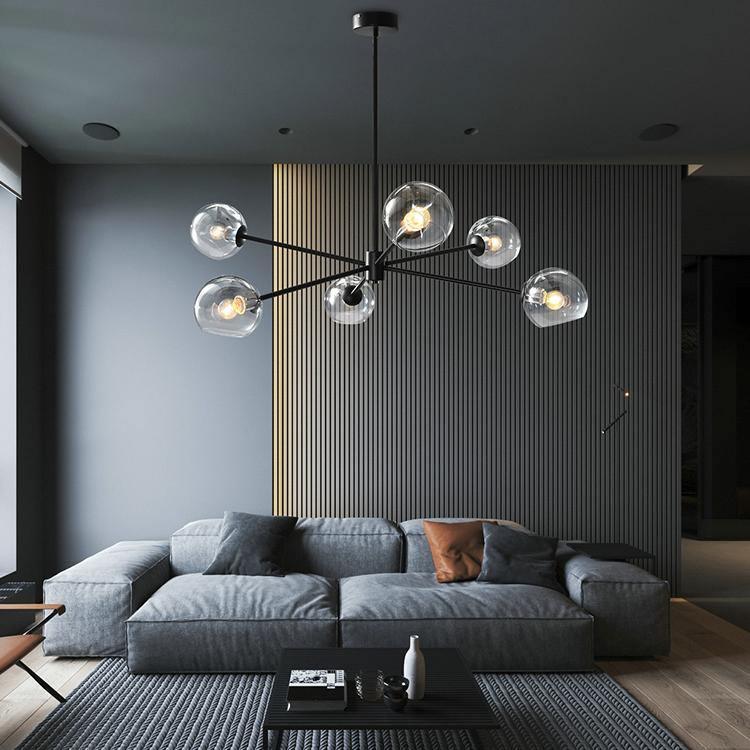 Black chandelier from Clérachic with clear glass globes and filament bulbs, above a grey sofa in front of a slatted dark wall.