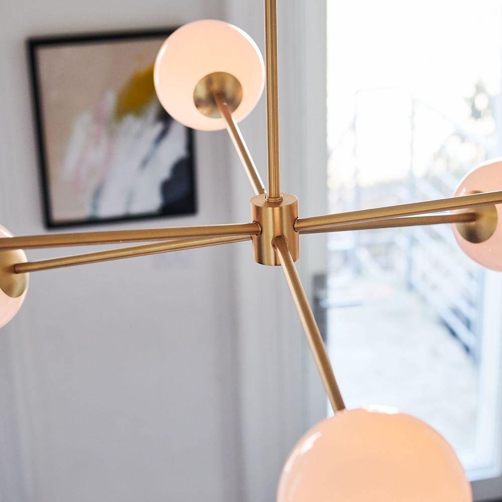 Close view of the gold hub and arms on this Clérachic chandelier, with two white globes glowing at the frame edges.