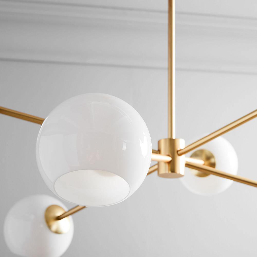 Close view of a white opal globe and the brass-coloured hub on this Clérachic chandelier, below a pale cornice.